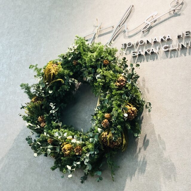 豊中駅前さかい内科・循環器クリニックの受付ロゴに飾られた、フレッシュグリーンのクリスマスリース。冬の季節感と温かい雰囲気を伝える院内装飾。