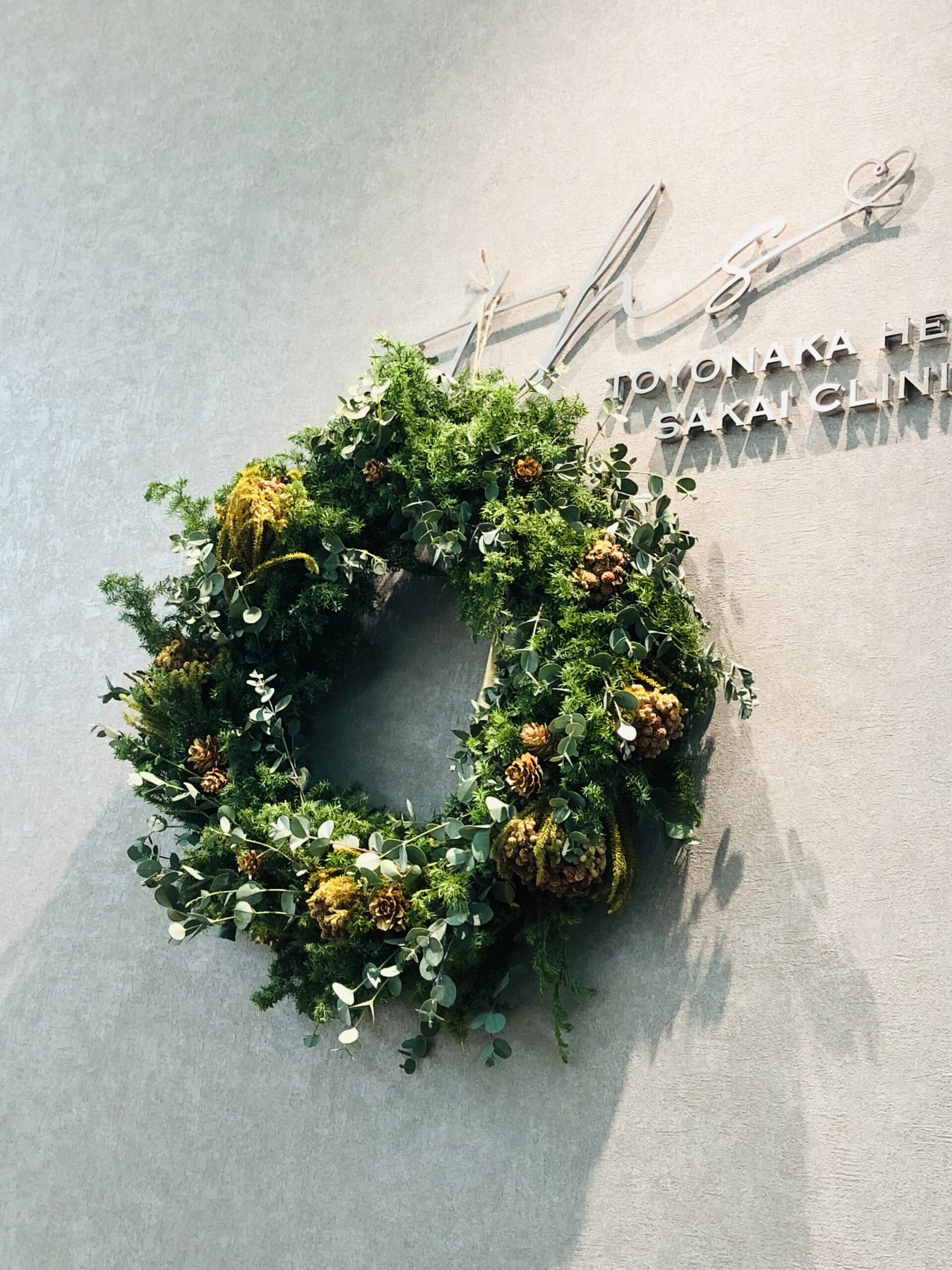 豊中駅前さかい内科・循環器クリニックの受付ロゴに飾られた、フレッシュグリーンのクリスマスリース。冬の季節感と温かい雰囲気を伝える院内装飾。